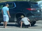 Mom with baby helps change a flat tire while husband watches