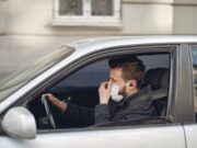 serious man in disposable mask and earbuds driving car at daytime