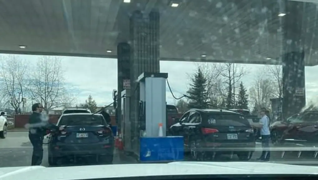 Customers at the Costco Gas station strech their hoses across their cars to reach the other side