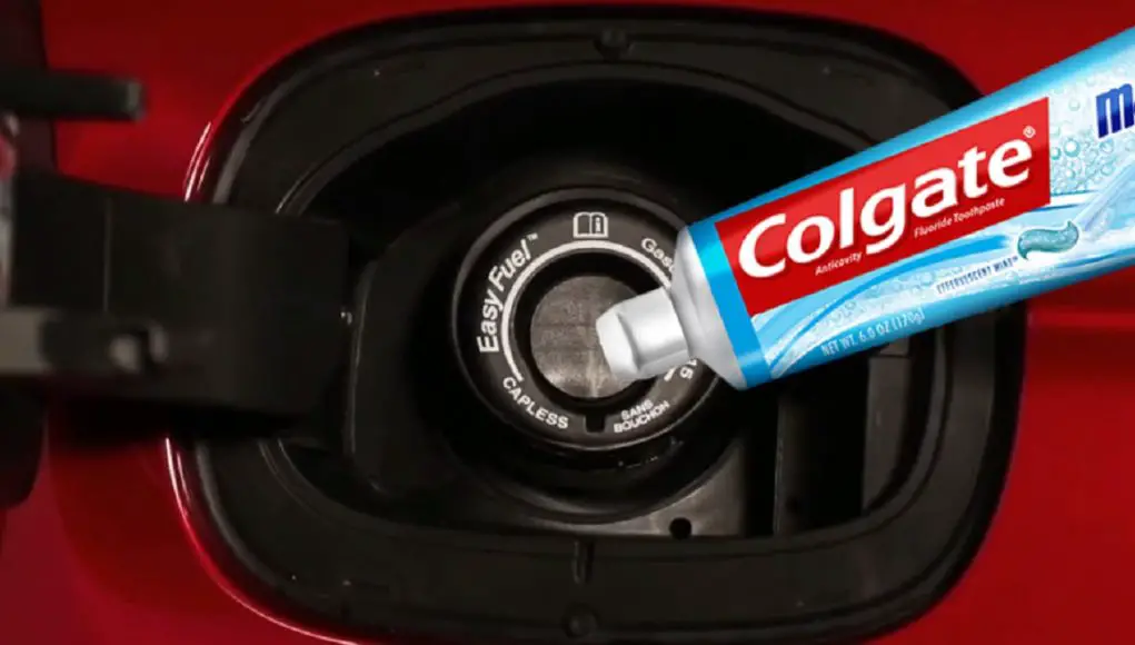 A tube of toothpaste in front of a fuel filler intake tube