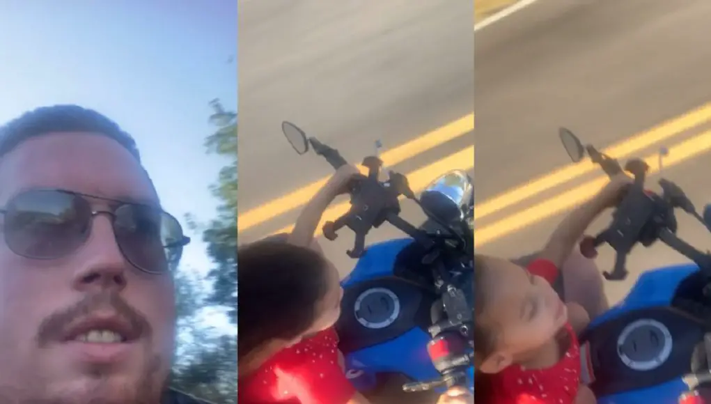 Dad films himself riding on his motorcycle, his daughter in front of him, both without helmets.