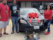 Two brothers standing next to a Car-Mart Ada rep with a crate of pitbull puppies in front of a Nissan Sentra.