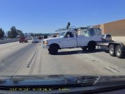 Driving towing dual axle flat bed trailer car hauler jackknifes performing simple lane change.